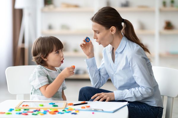 Woman and child playing with colorful shapes, child imitating woman's mouth movements. Interior setting.