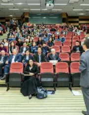 Professor giving a lecture to a large audience in a tiered auditorium.