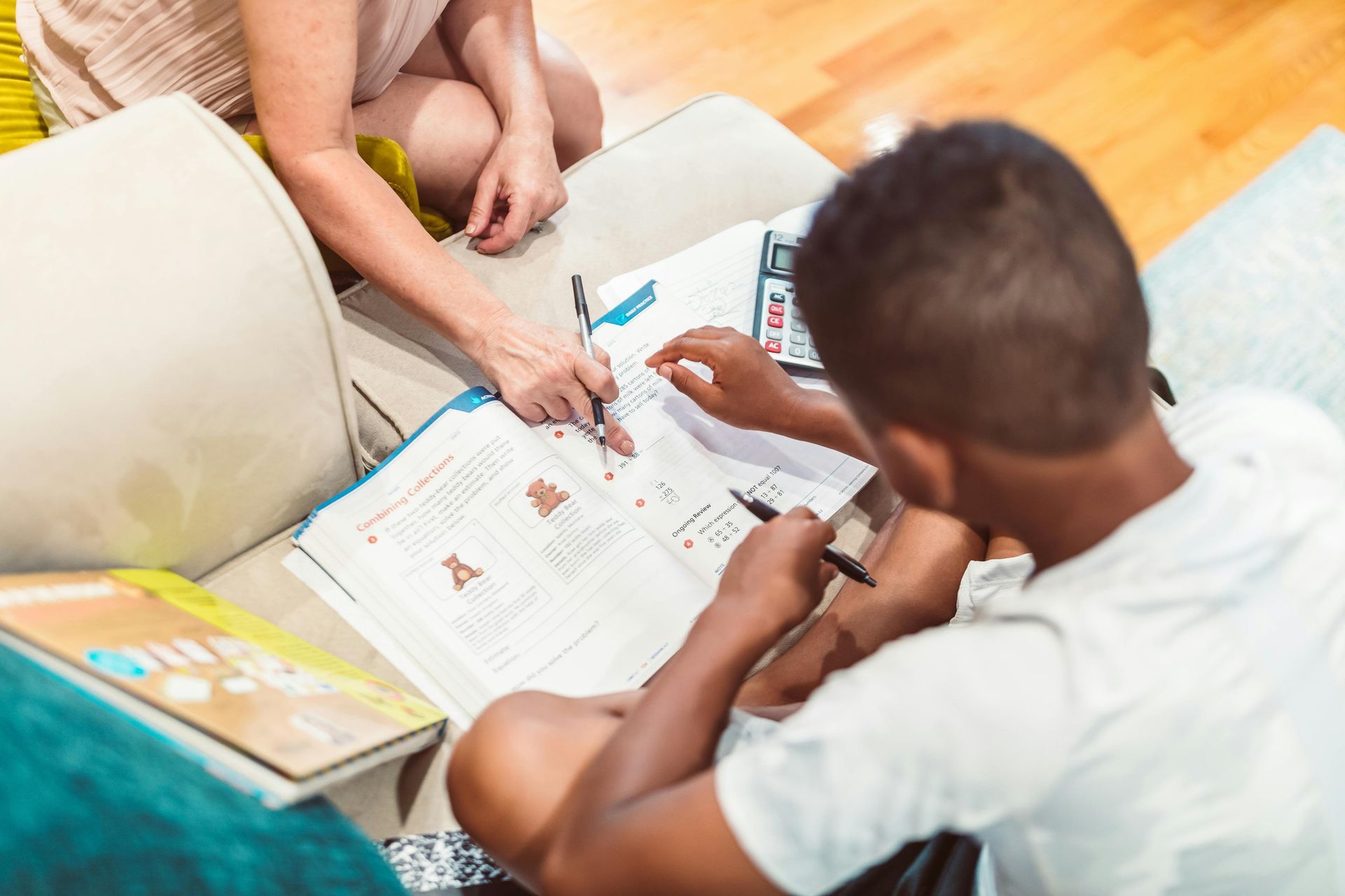 Woman and boy at a table, making a heart shape over a drawing. Tools and art supplies are nearby.