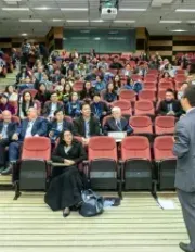 Professor giving a lecture to a large audience in a tiered auditorium.