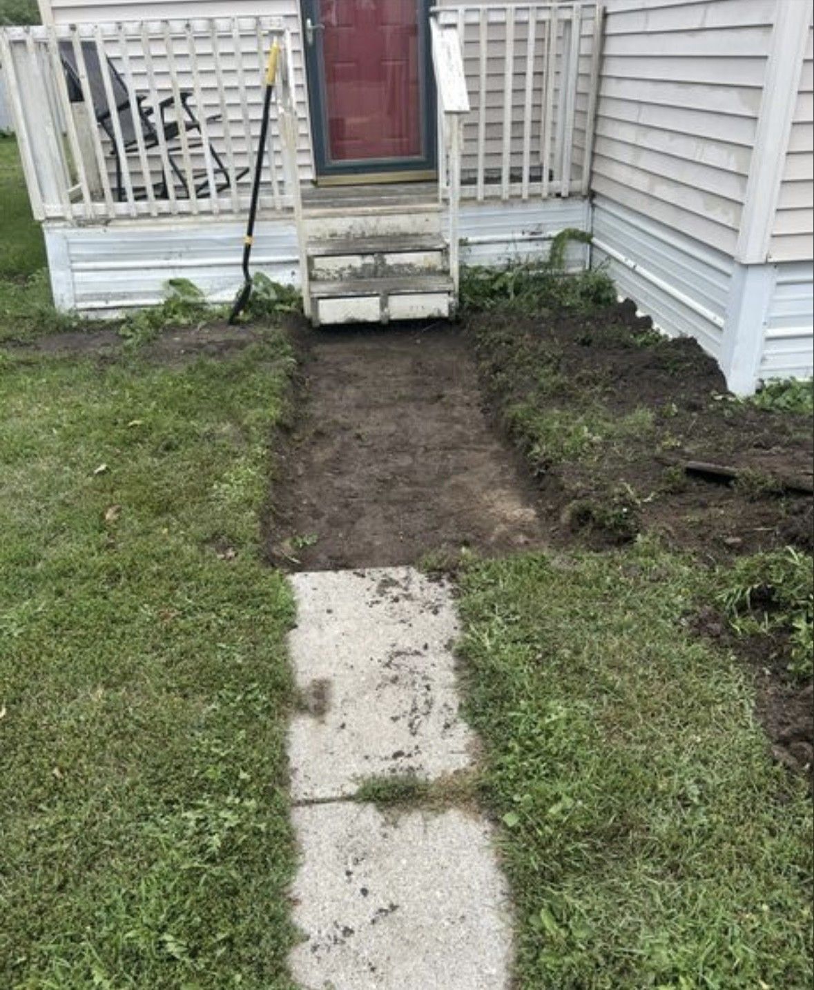 A short, worn concrete sidewalk leading to the dirt-cleared area in front of house steps and a porch.