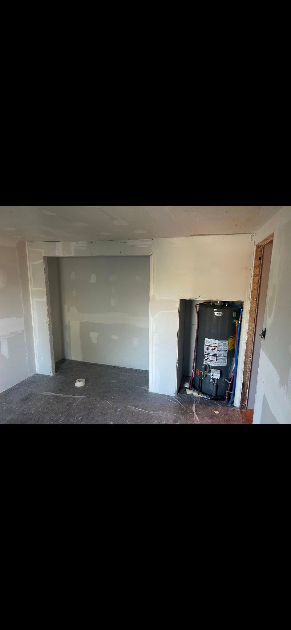 A room under renovation with drywall installed, a recessed wall opening, and a utility cabinet exposed on the right.
