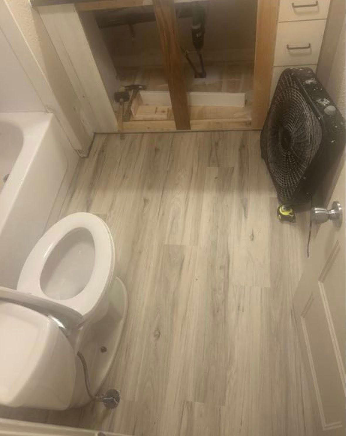 A bathroom undergoing a renovation, featuring light wood-look flooring, a toilet, and an empty vanity frame.