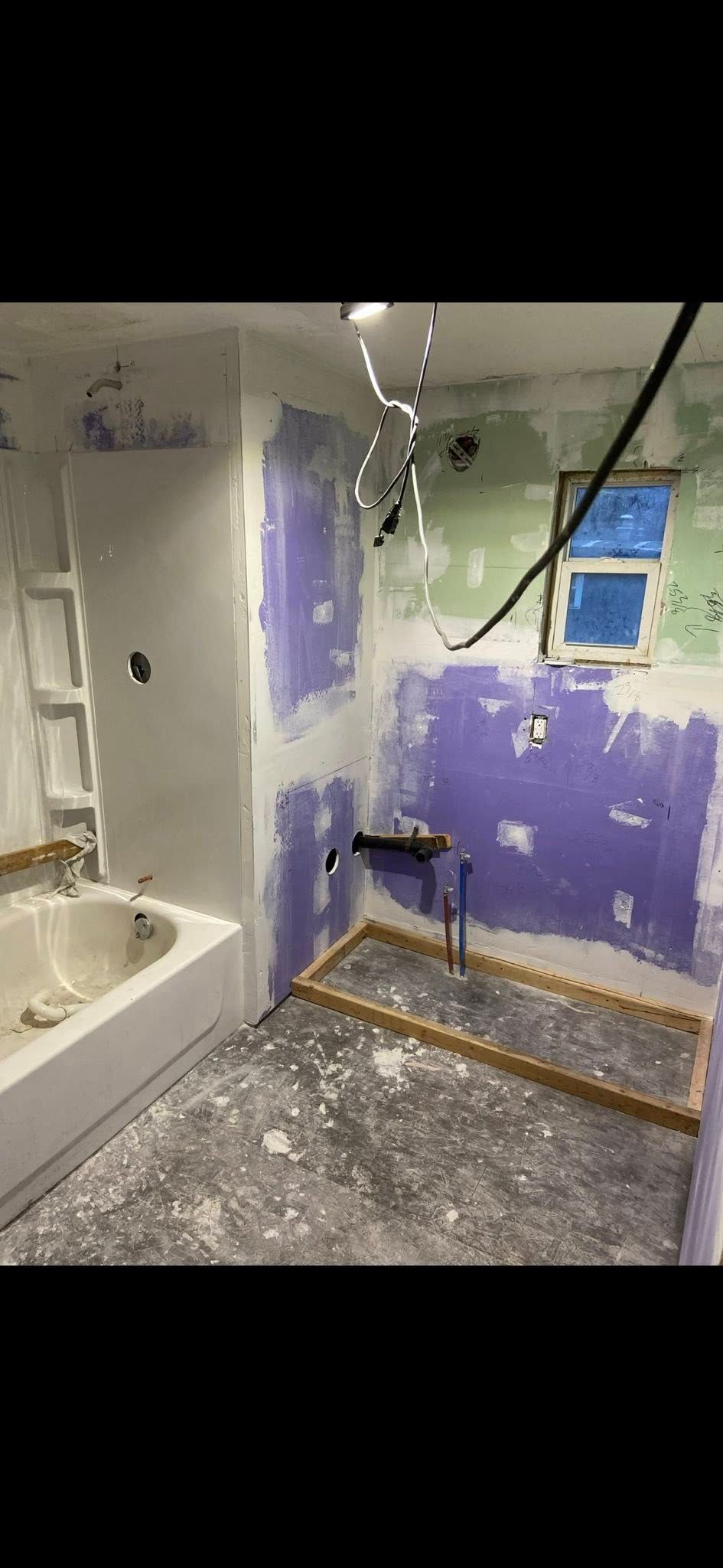 A bathroom undergoing renovation featuring a bathtub, purple moisture-resistant drywall, and a framed shower base.