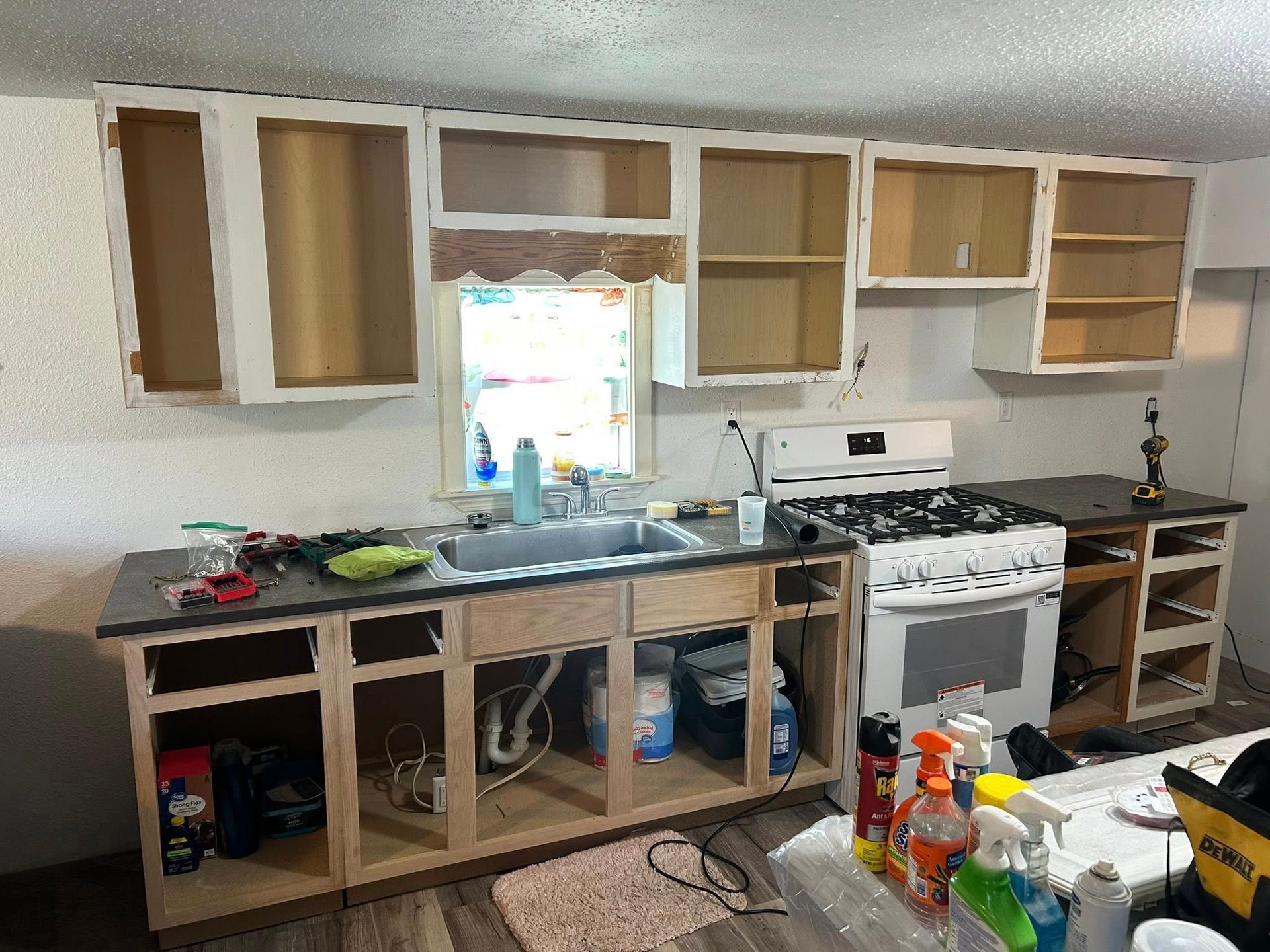 A kitchen undergoing renovation with white-painted upper cabinets, missing cabinet doors, and a stove in place.