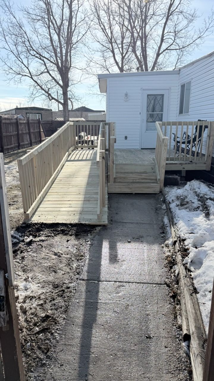 A wooden wheelchair ramp and short staircase leading to the entrance of a white house on a sunny day.