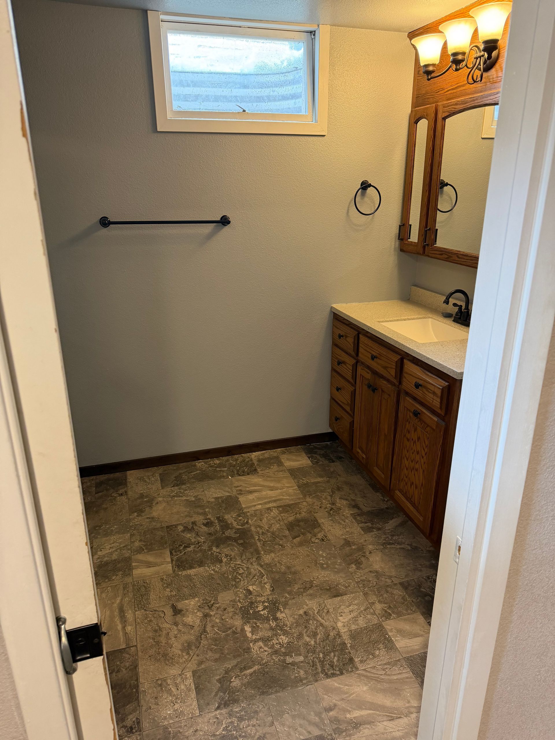 Empty bathroom with vanity, mirror, window, towel bar, and gray tiled floor.