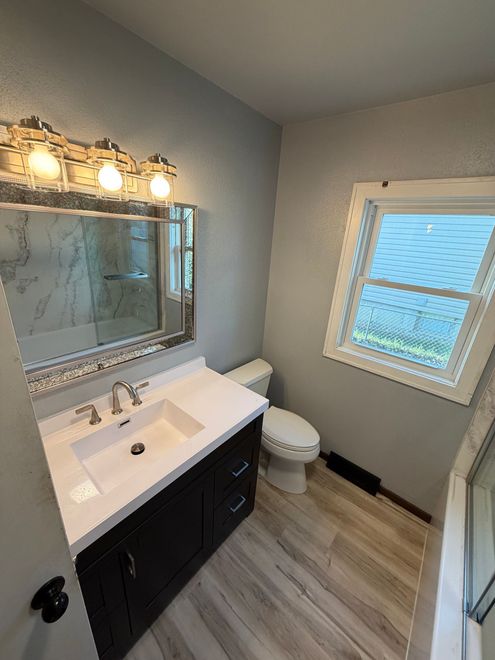 Small bathroom with vanity, mirror lights, toilet, and window with blinds.