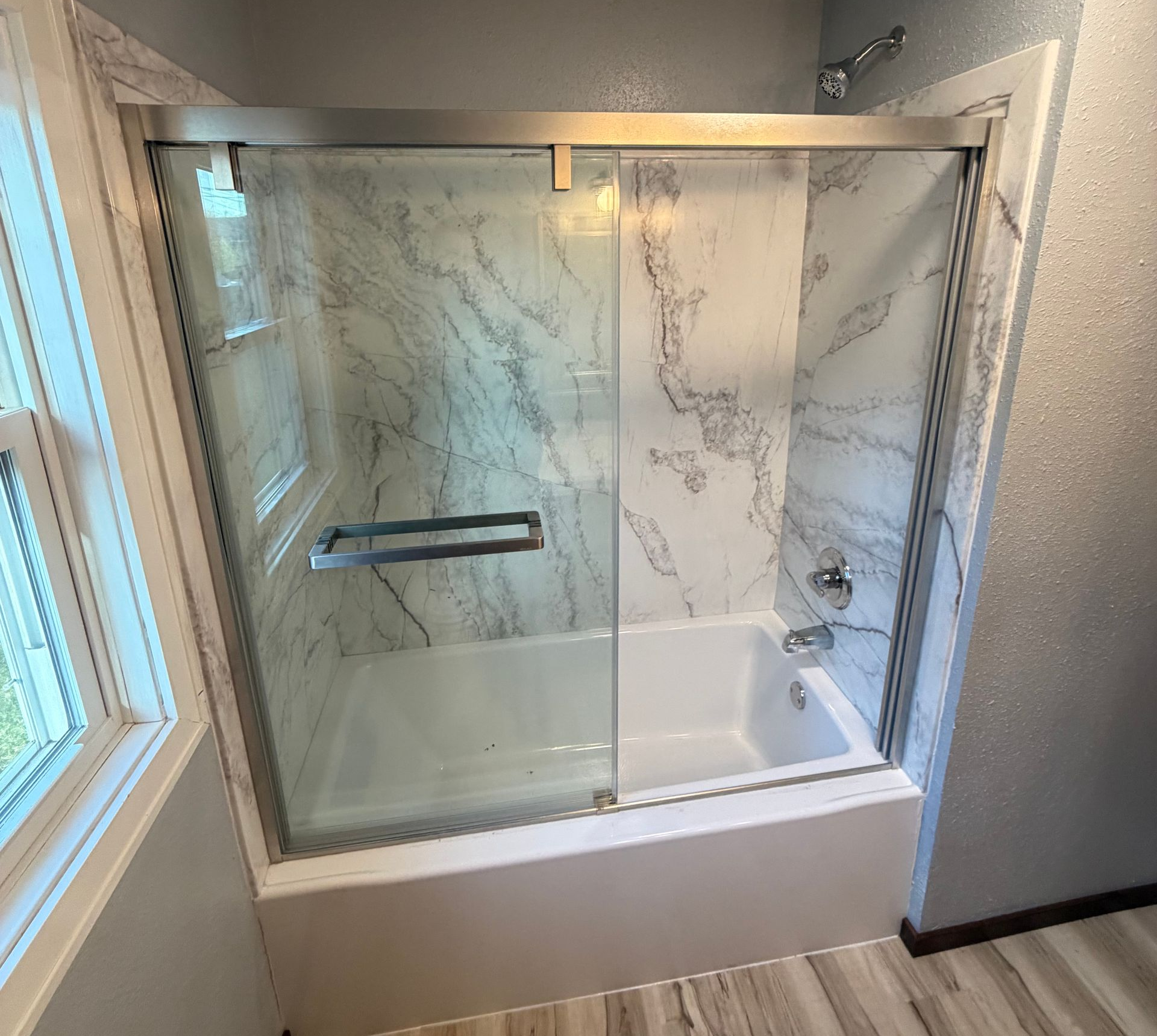 Modern bathroom with glass shower, marble-look tile, and white tub surround