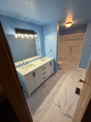 Blue bathroom with white vanity, lit mirror, marble-look floor, and shower stall in the back.