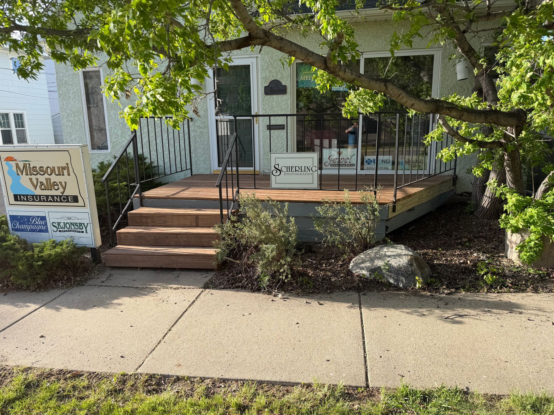 Front porch entrance with steps, railing, and a “Harmony Village” sign by the sidewalk