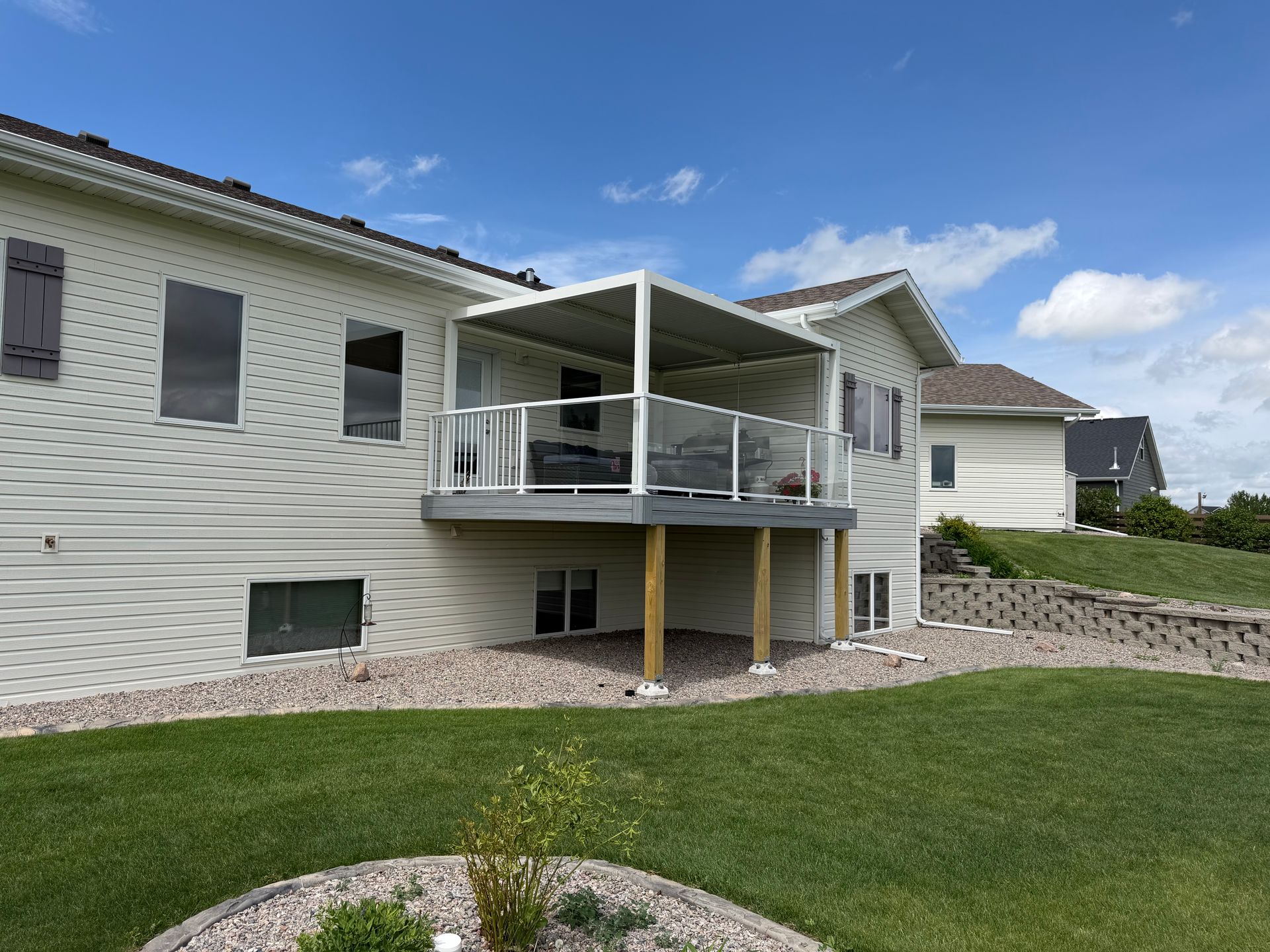 Back patio deck on a white house with glass railing and grassy yard