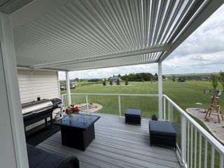 Covered patio with black furniture, striped rug, and open view of a grassy yard and cloudy sky