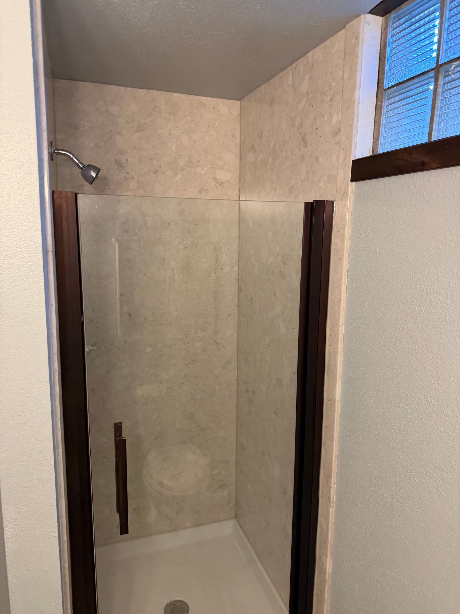 Small beige walk-in shower with dark trim and a window above the wall.