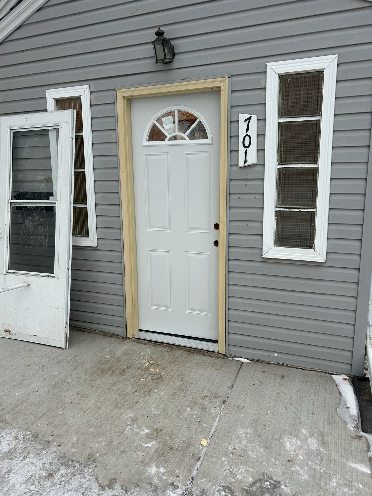 A gray house exterior with a white door, a detached door frame leaning to the left, and address number 4101.
