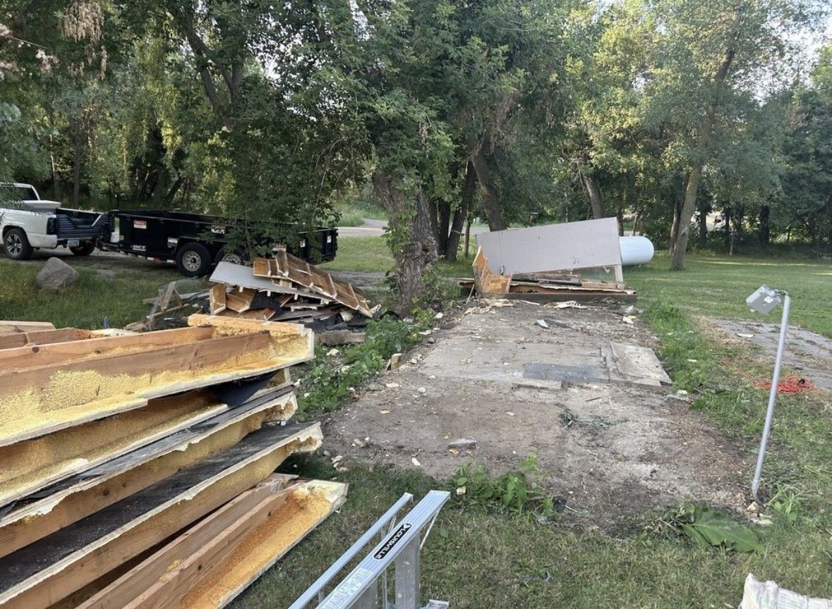 A construction site with stacked lumber in the foreground and the concrete foundation of a demolished building beyond.