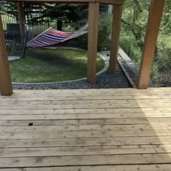 A view from a wooden deck looking out toward a backyard with a colorful striped hammock hanging under a wooden structure.