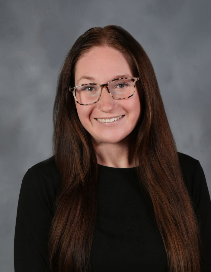 Woman with long brown hair, glasses, and black shirt smiles.