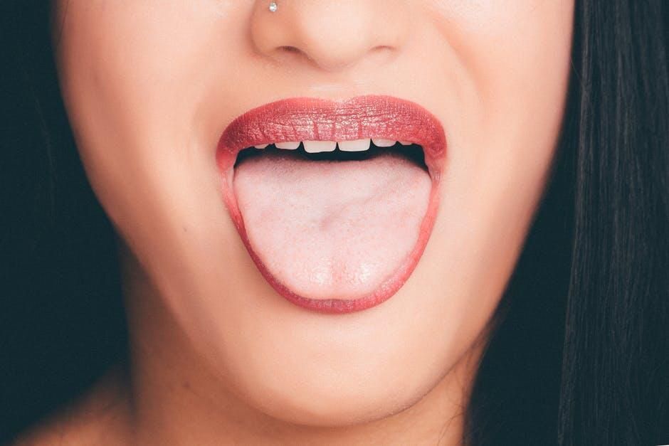 Close-up of a person sticking out a tongue with glossy pink lips and a nose piercing