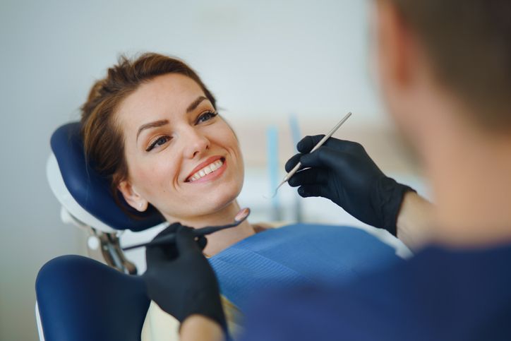 Smiling woman's teeth examined by hands in blue gloves.