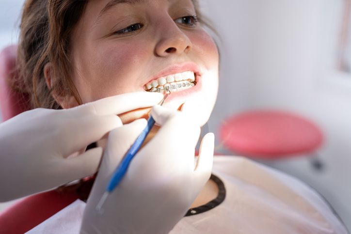 Woman smiling in a dental chair as dentist examines her teeth with instruments.
