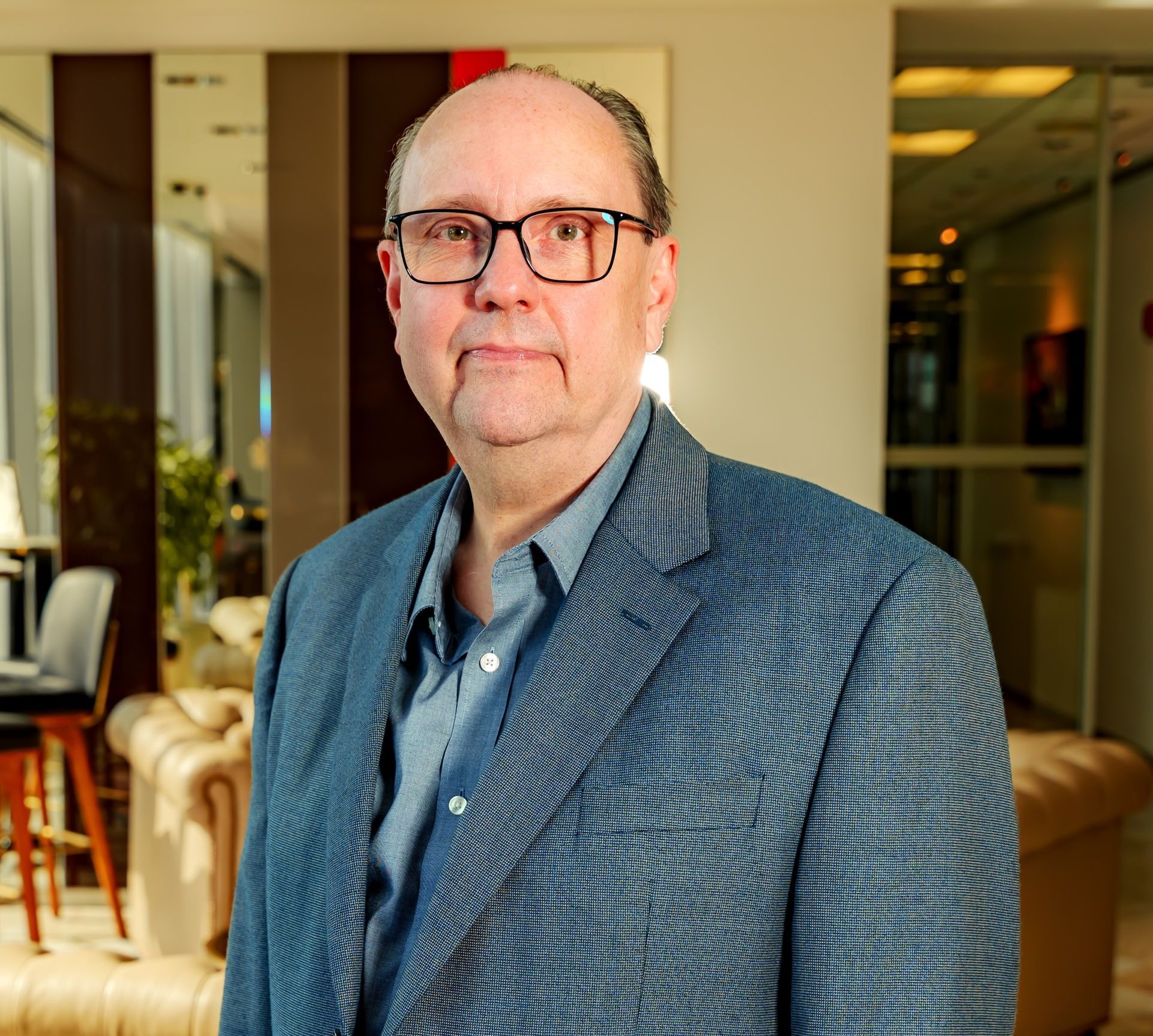 Man in blue jacket and glasses in an upscale interior setting.