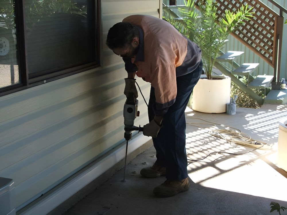 A Man is Using a Hammer to Drill a Hole in a Wall — Audy Geiszler Pest Control in Cannonvale, QLD