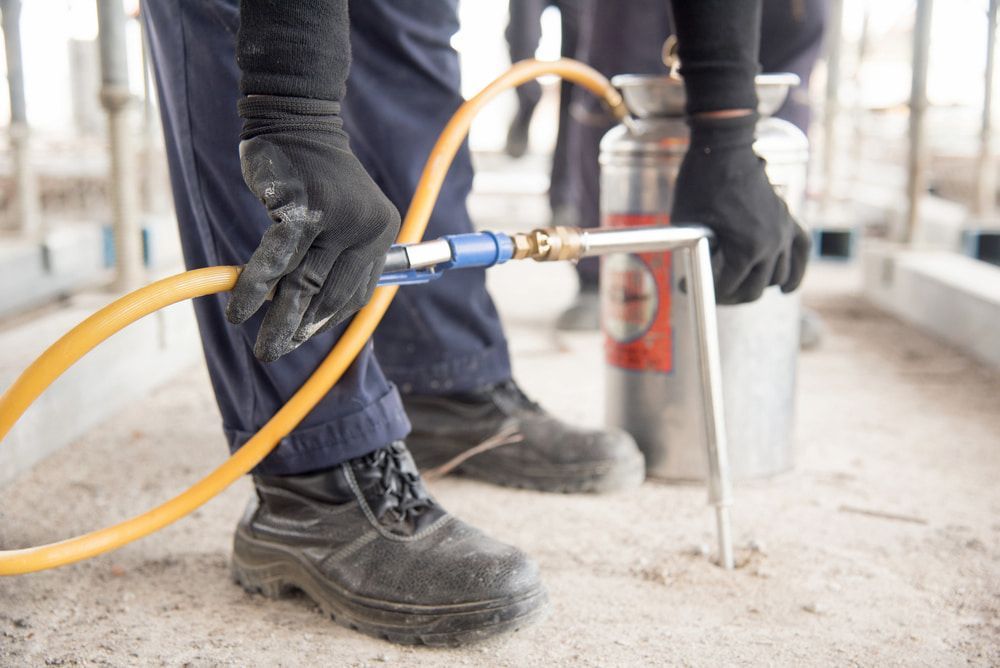 A Man is Spraying a Hose With a Sprayer — Audy Geiszler Pest Control in Collinsville, QLD