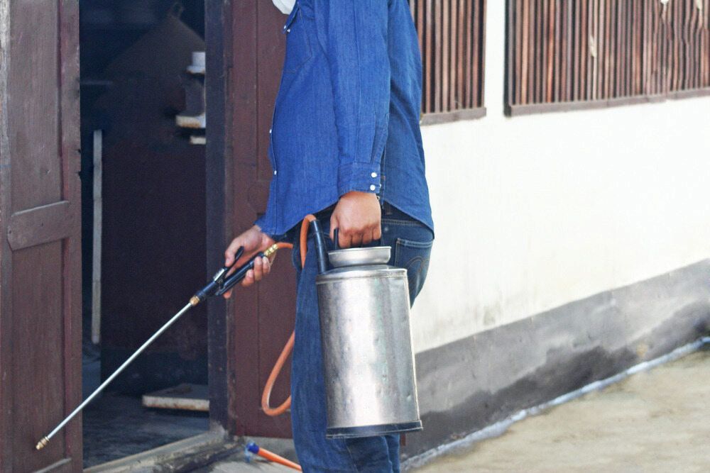 A Man is Spraying a Building With a Sprayer — Audy Geiszler Pest Control in Collinsville, QLD