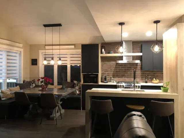 Cuisine moderne avec coin repas. Armoires noires, mur en briques, tabourets de bar et suspensions.