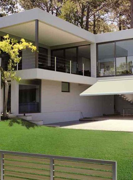 Moderna casa a due piani con ampie finestre e prato verde. Tende da sole che si estendono sul patio.