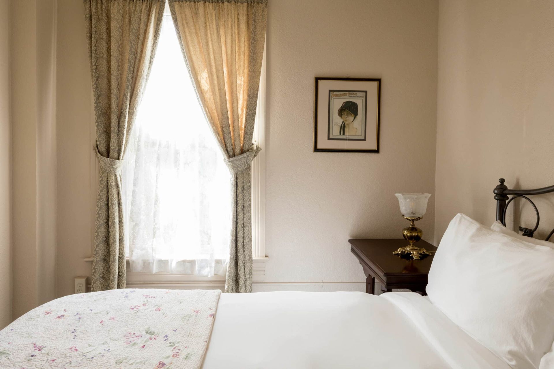 A bedroom with a bed , nightstand , lamp and window.