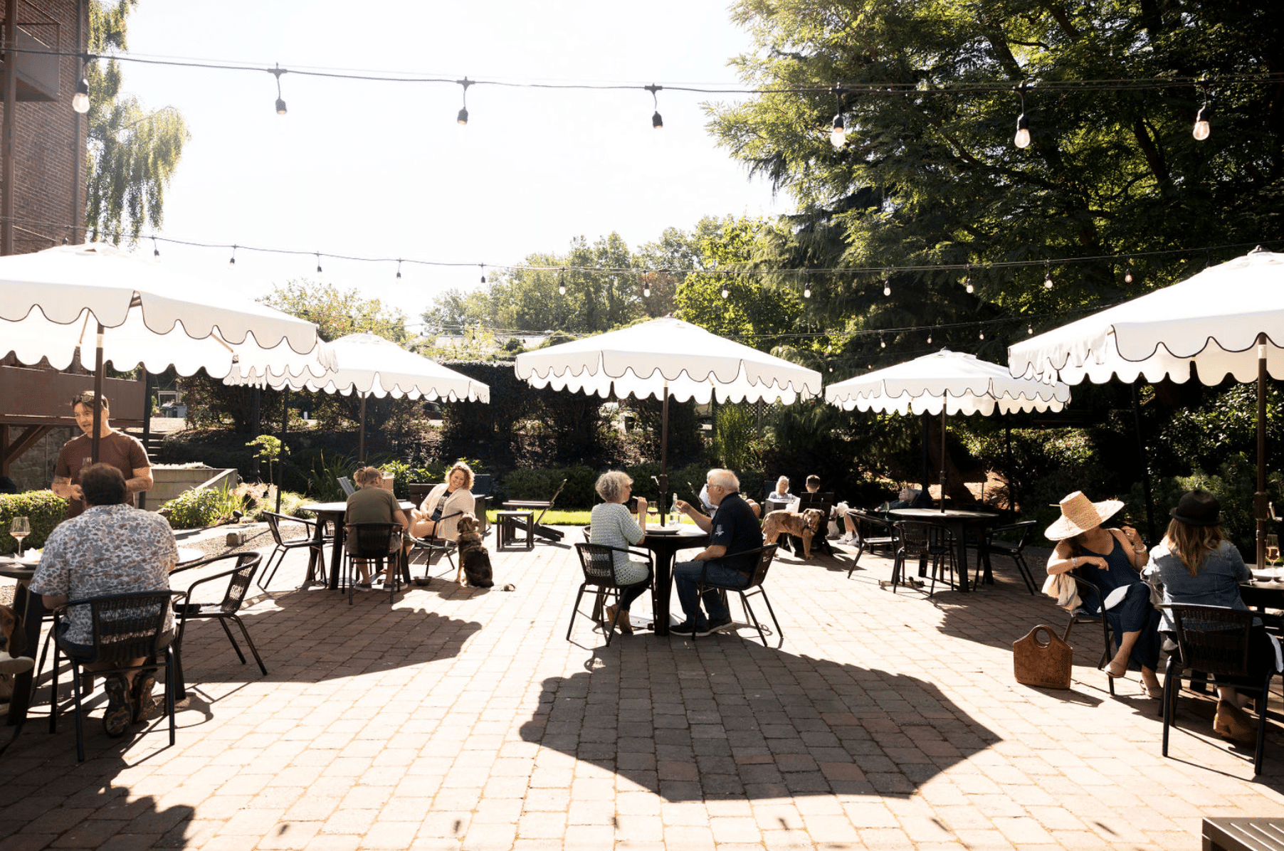 A group of people are sitting at tables under umbrellas on a patio.