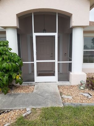 Exterior view of a home's entrance with a screen door, columns, and a walkway.