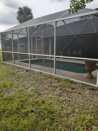 A screened-in pool enclosure with a rectangular pool, located behind a house on a grassy lawn.