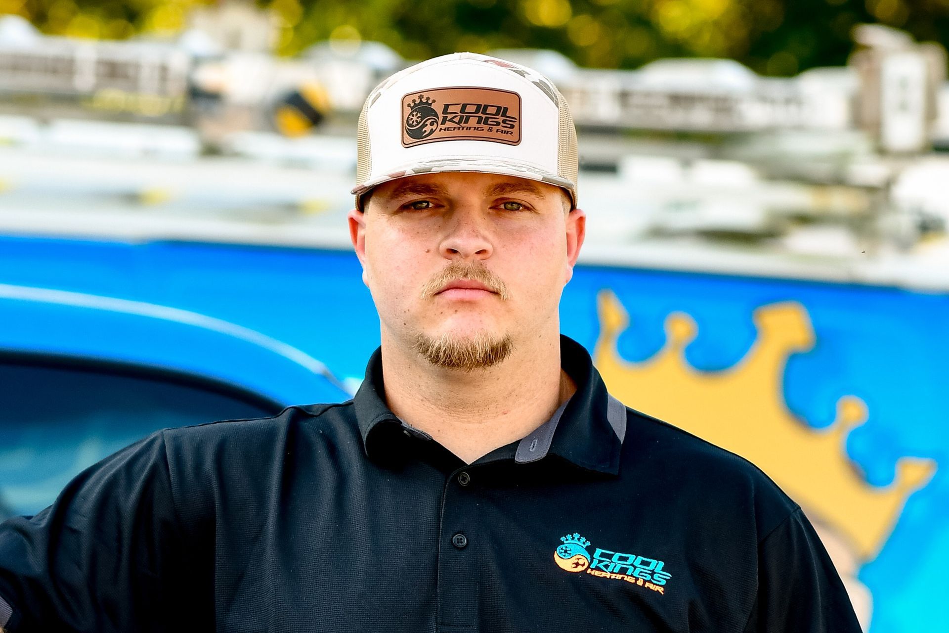 Man standing in front of a blue vehicle with a yellow crown graphic, wearing a black shirt and white cap.