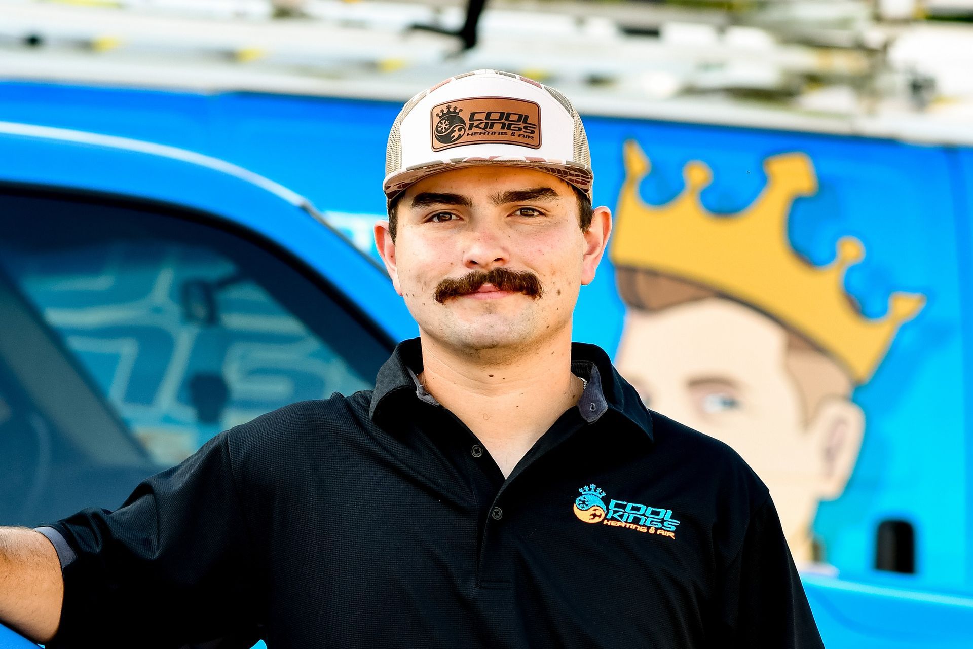 Man in black shirt and cap standing by a blue truck with a crown logo