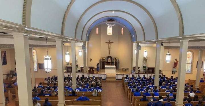 Church interior filled with people wearing blue, seated in wooden pews.
