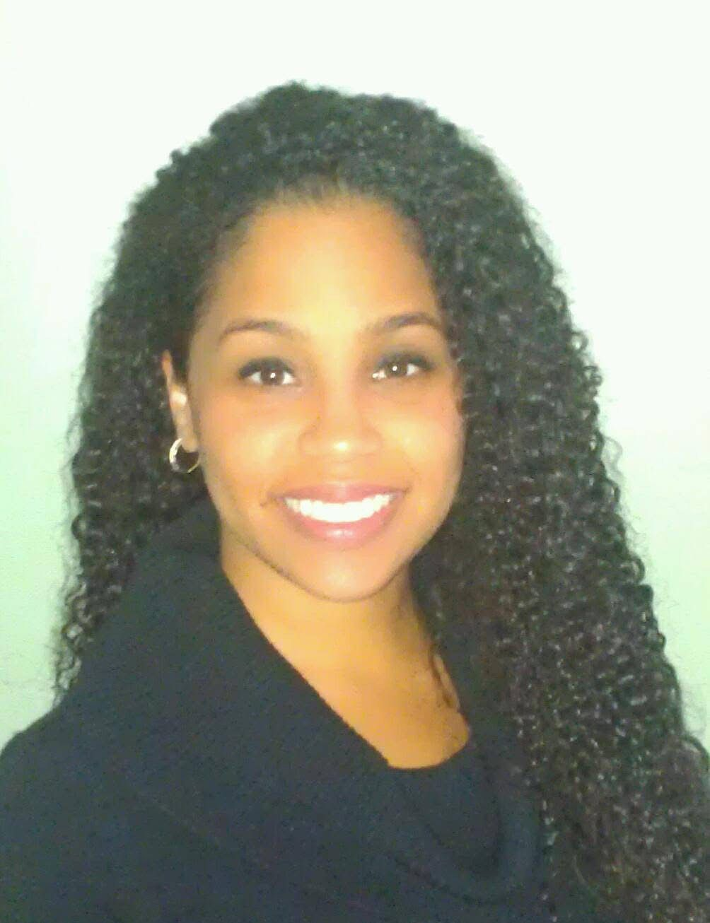 Smiling woman with long, curly dark hair wearing a black top.