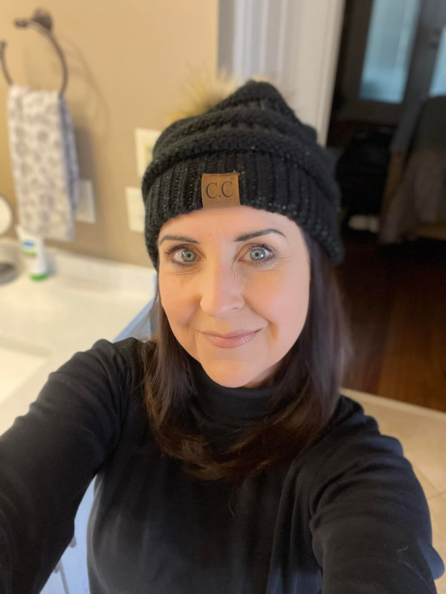Woman in black hat and turtleneck takes a selfie in a bathroom.