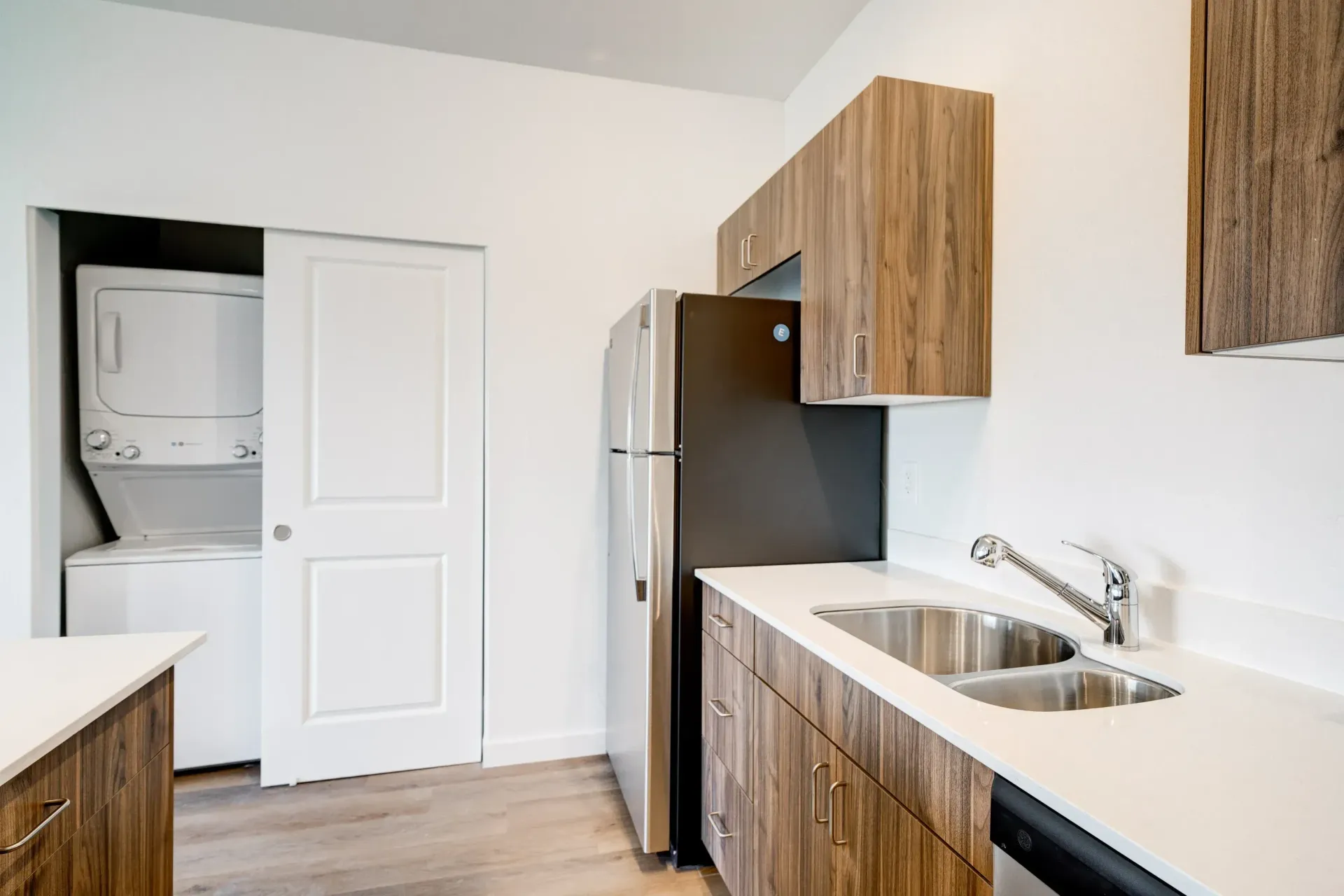Kitchen area with double sink, wood cabinets, refrigerator, and stacked washer/dryer in a closet.