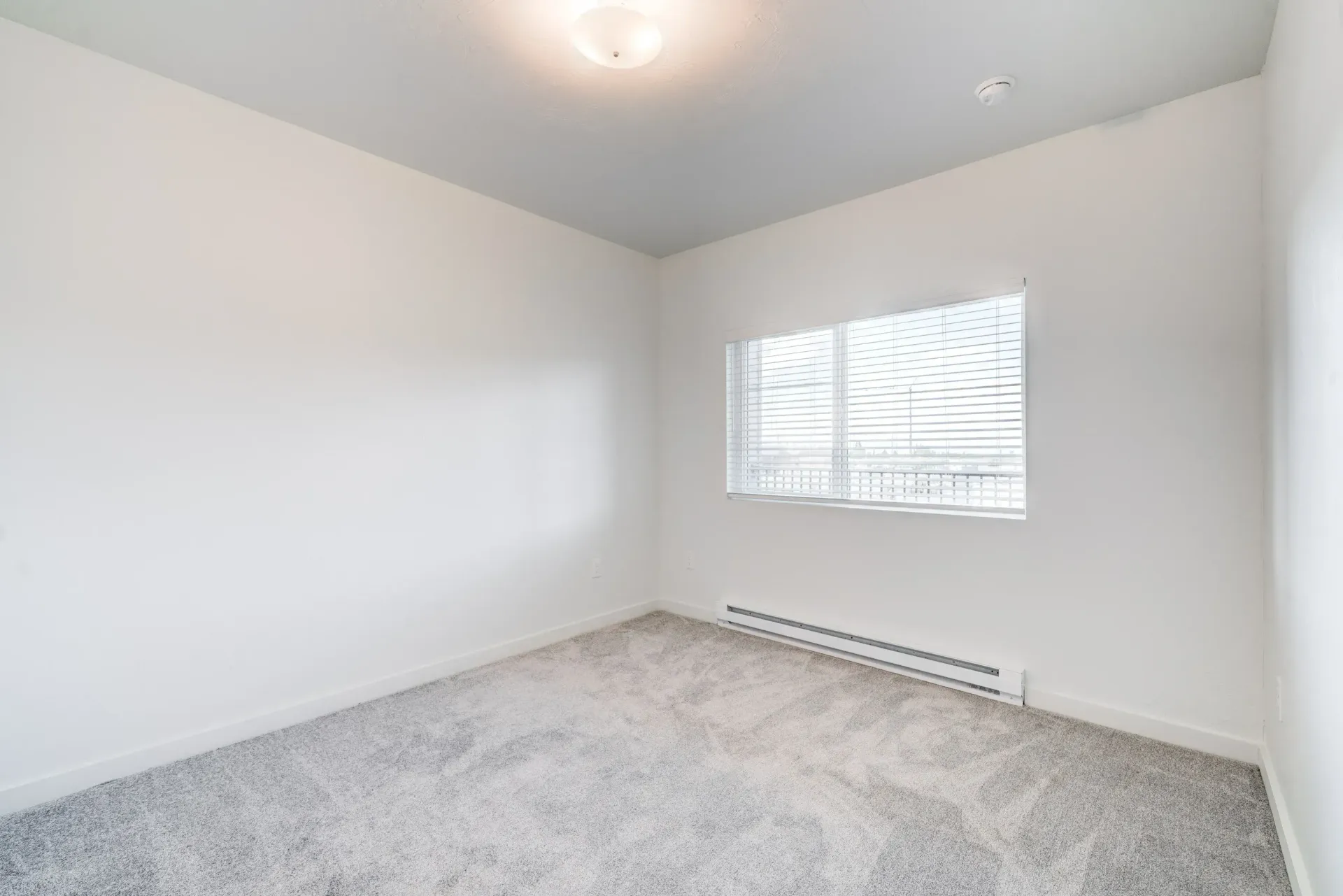 Empty bedroom with white walls, a window with blinds, and a baseboard heater.