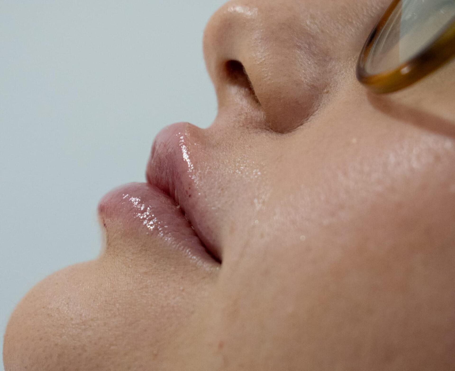 Primer plano del perfil de los labios y la nariz de una persona, mostrando la textura natural de la piel y un ligero brillo.