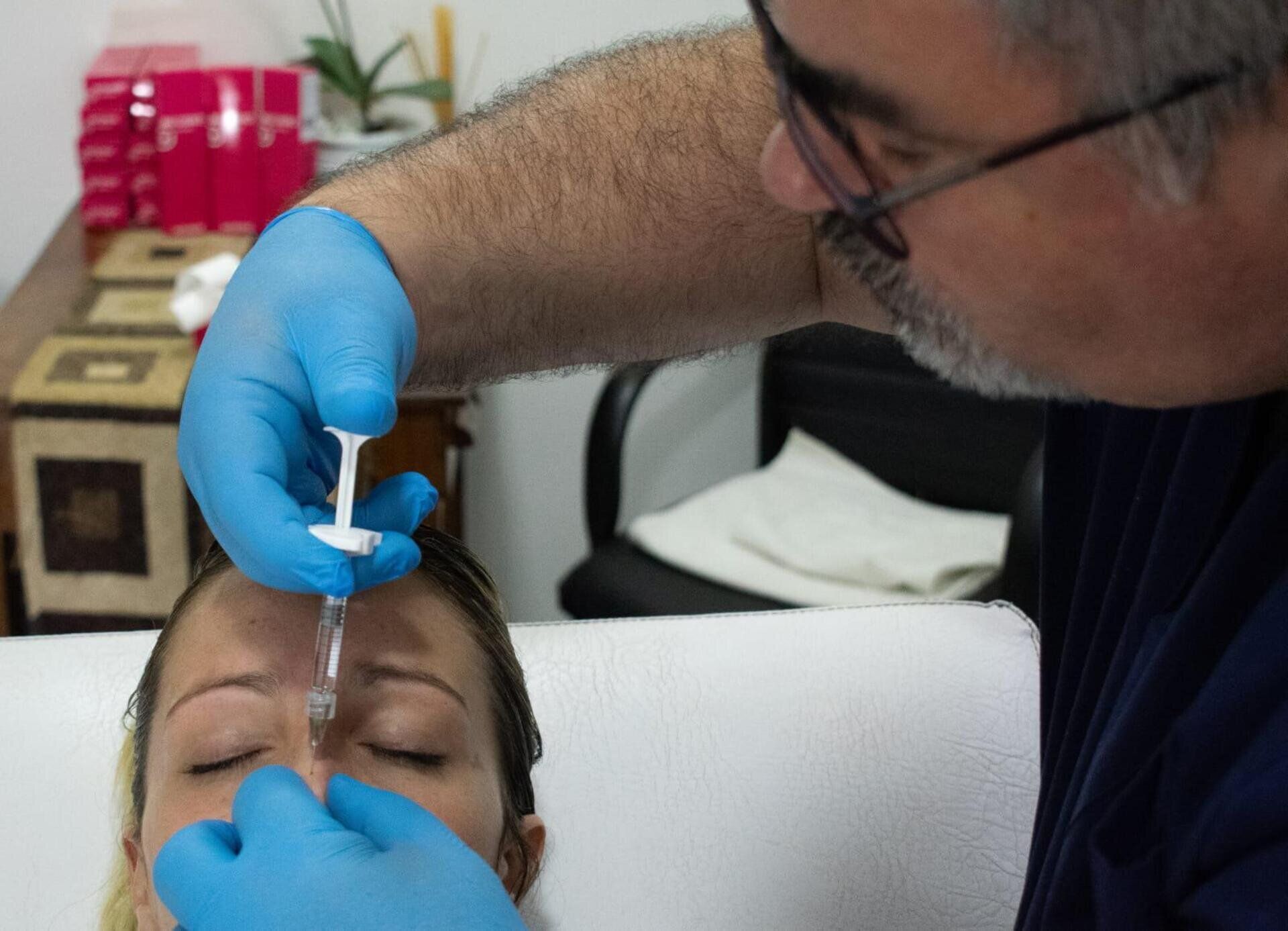 Un profesional sanitario, con guantes azules, administra una inyección en el puente de la nariz