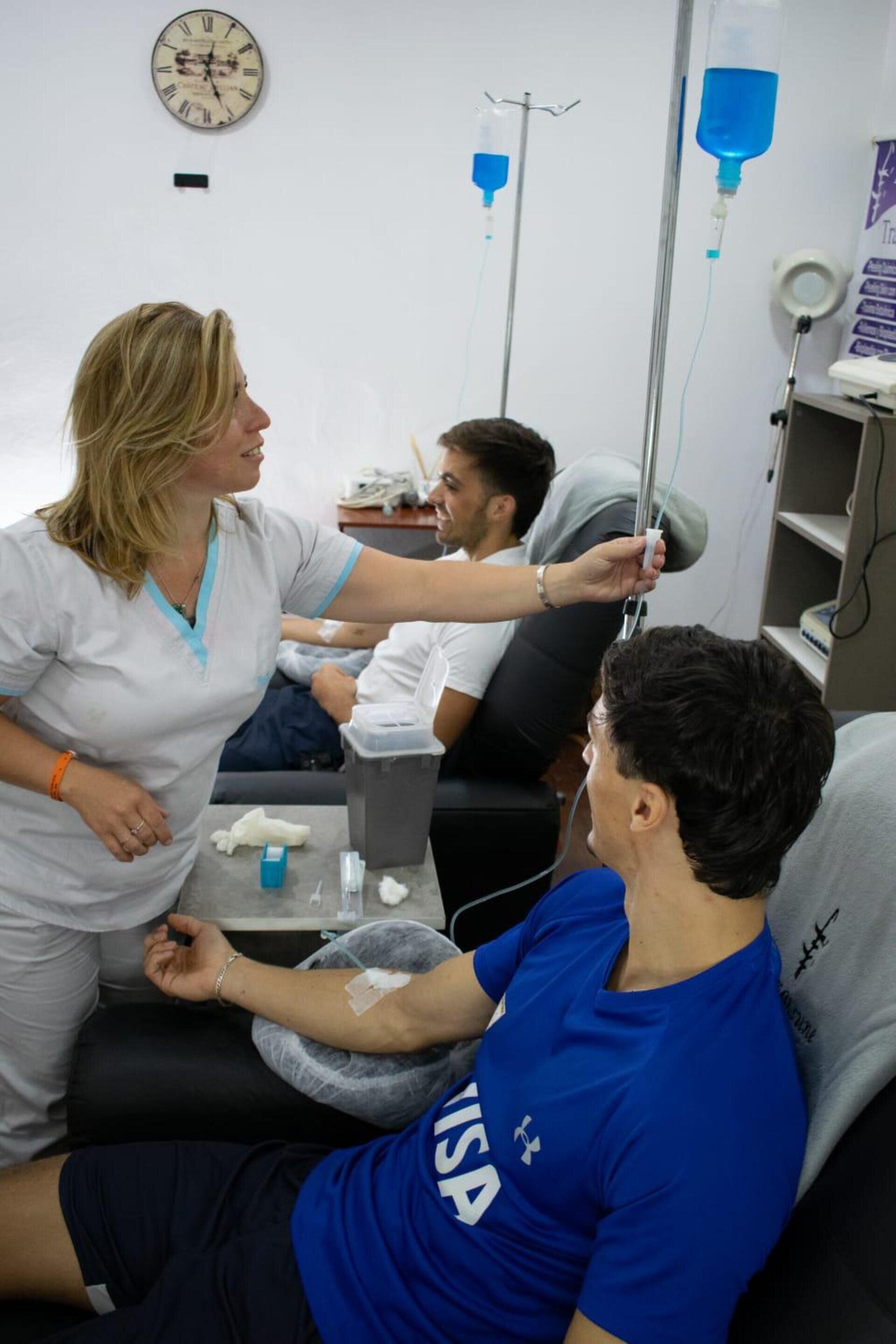 Un profesional sanitario ajusta una vía intravenosa con líquido azul para un paciente en una sala de tratamiento clínico.