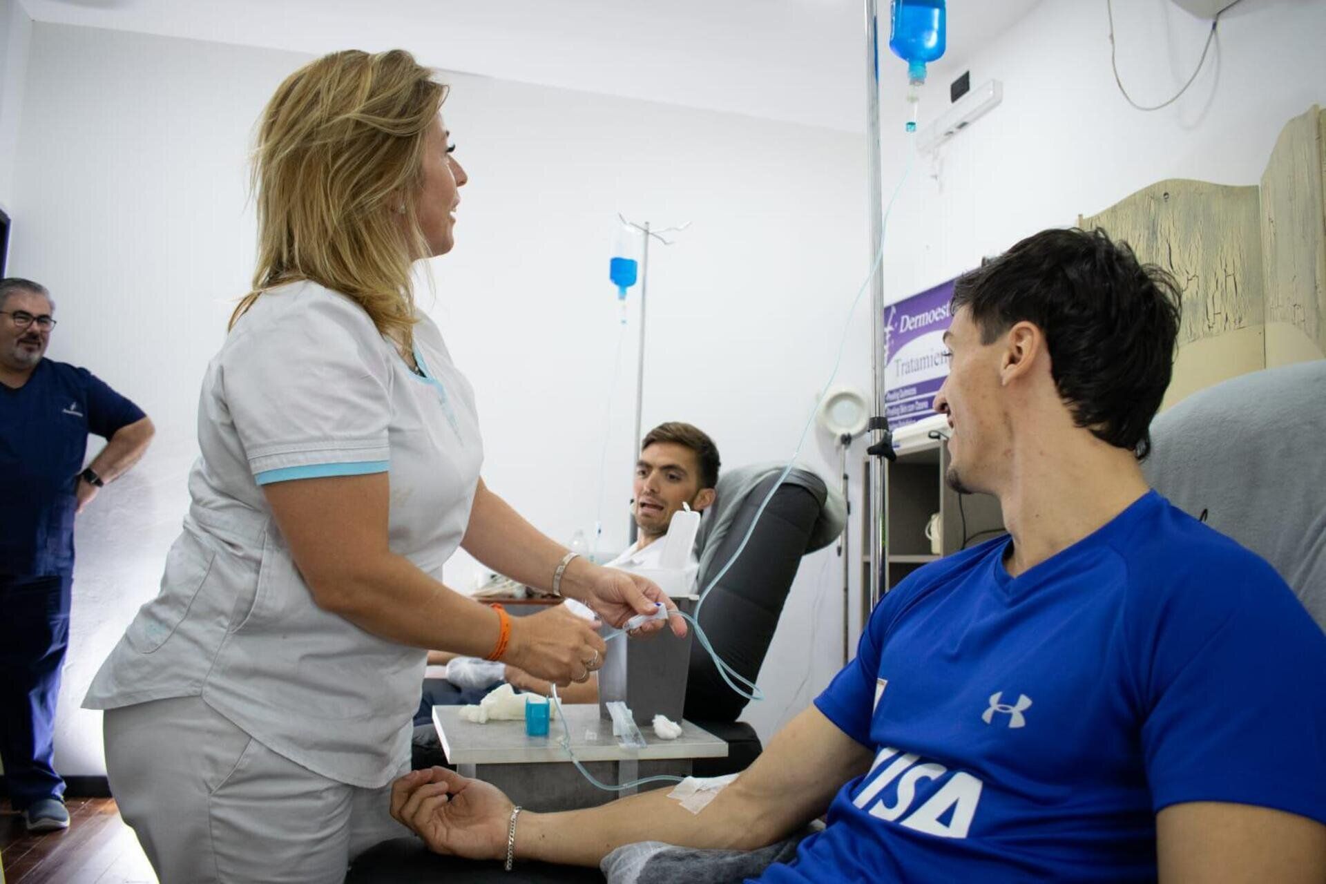 Una enfermera prepara una vía intravenosa para un atleta con una camiseta azul en una clínica