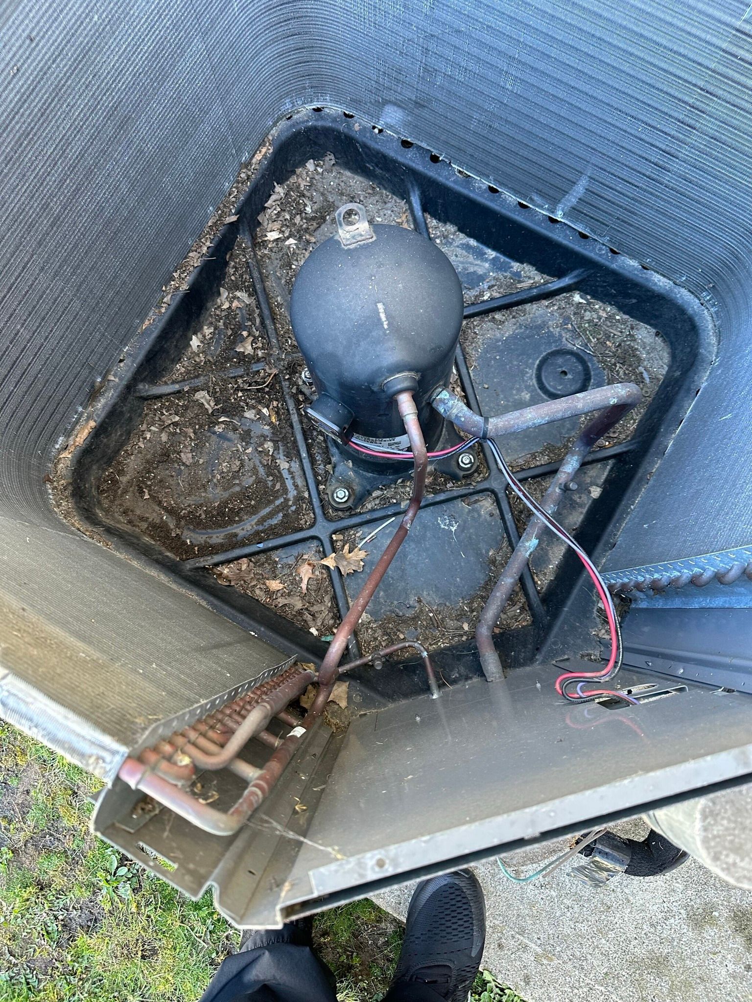 Top-down view of an air conditioner unit's interior with a compressor, copper tubing, and debris in the base.