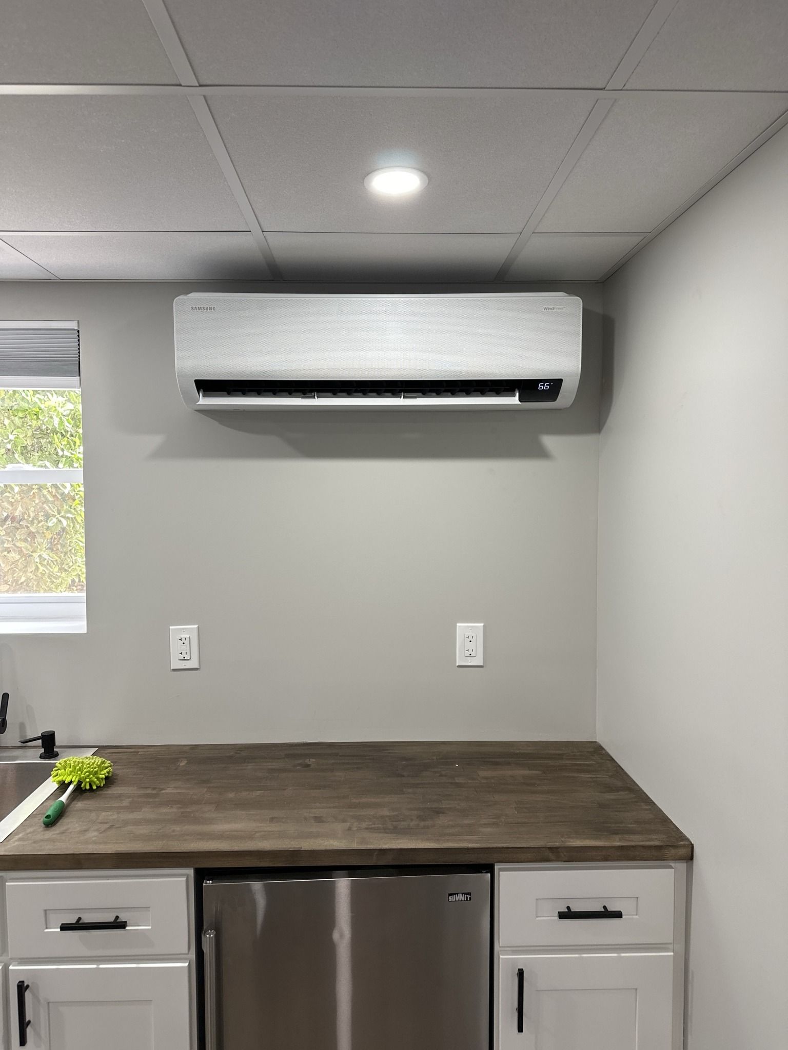 Mini-split air conditioner mounted on a gray wall above a counter with a refrigerator.