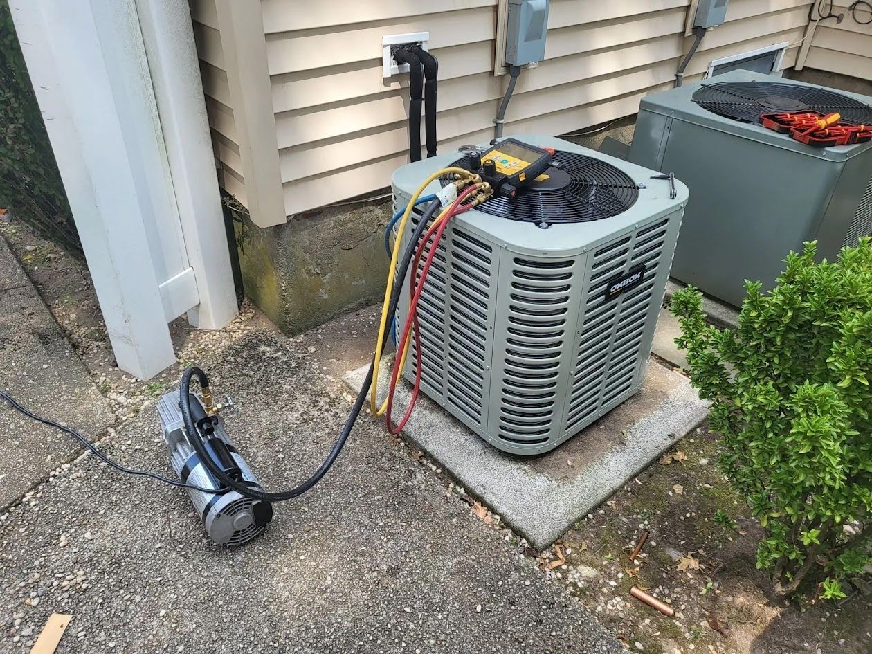 HVAC unit with gauges and a vacuum pump connected, outside a house.