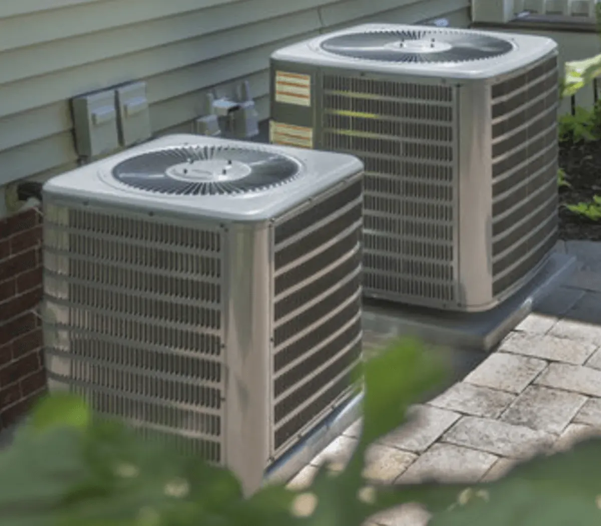 Two air conditioners are sitting outside of a house.